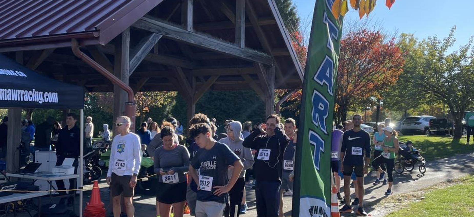 A crowd gathered at a running event with a start banner outdoors.