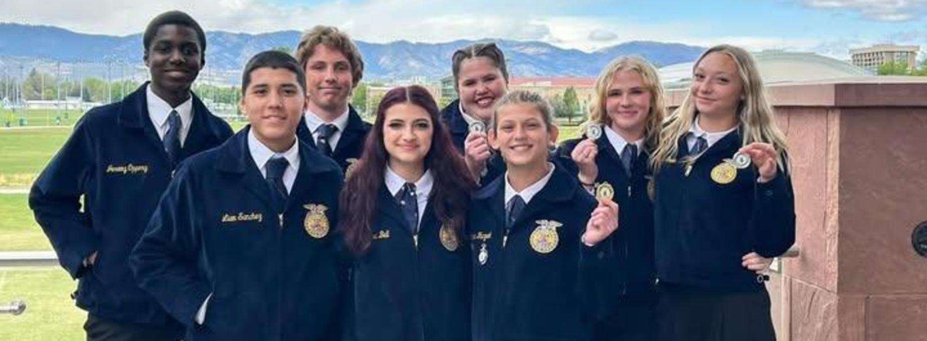 FFA members displaying medals outdoors with mountains in the background.