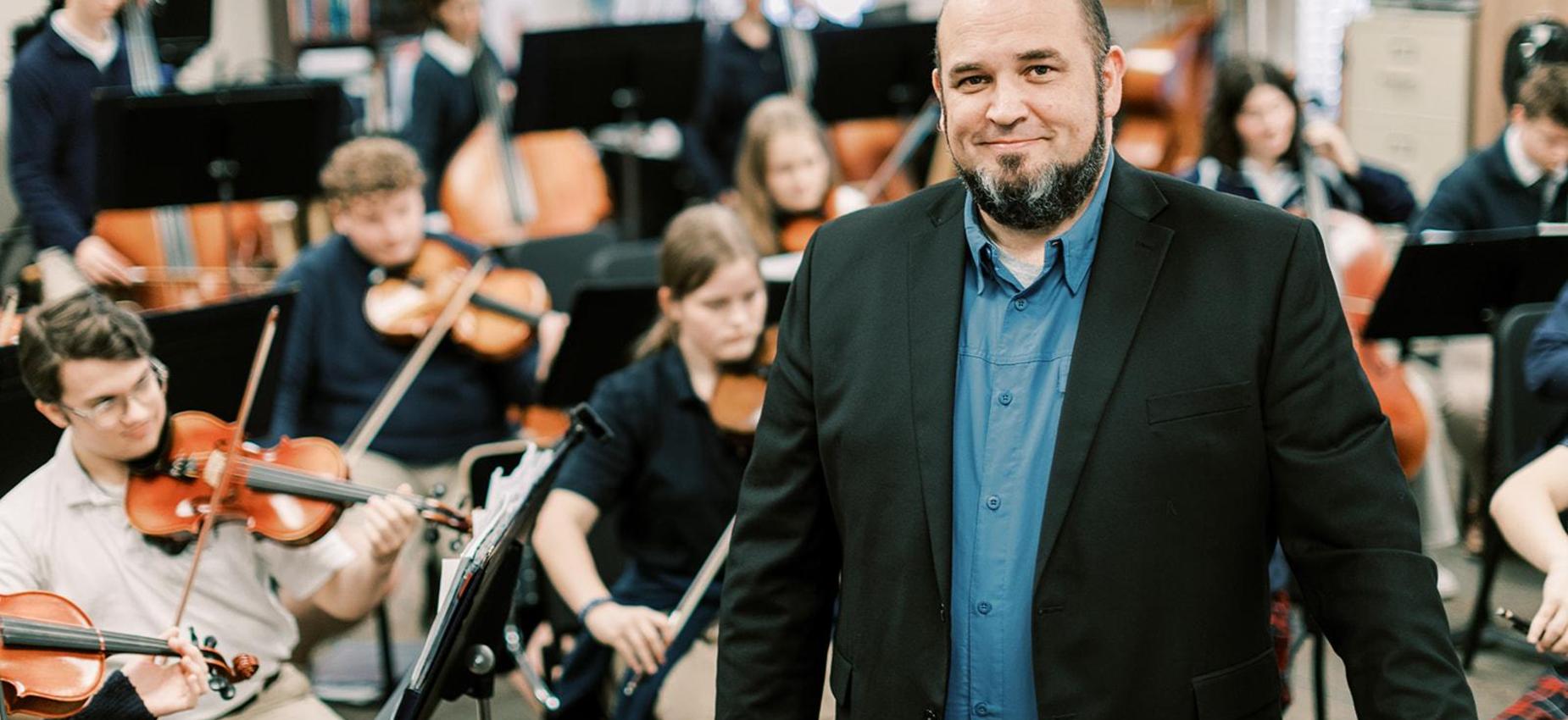 Orchestra teacher smiles in front of his student musicians