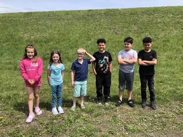 Six children standing in a line on grass, smiling and posing together.