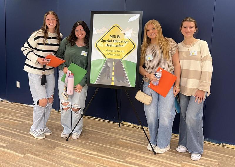 Four girls standing on either side of a poster on a stand