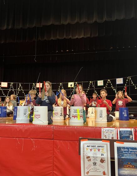 Students performing with buckets on stage during a school event.