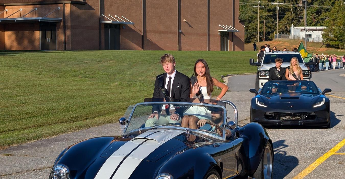 A group of students in formal attire parading in luxury cars.