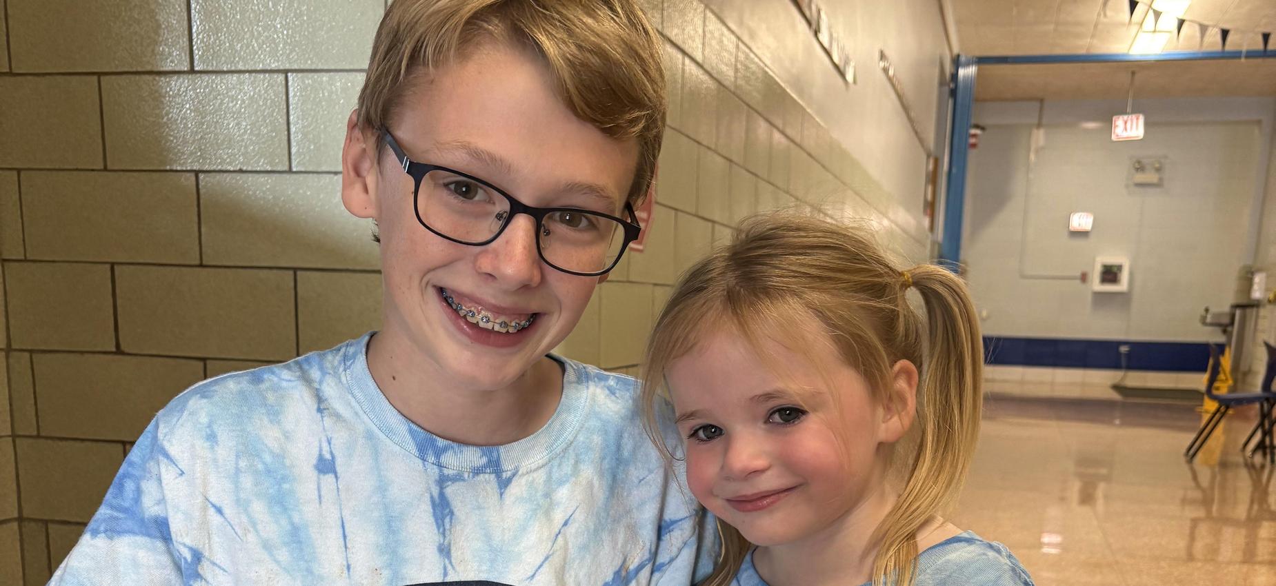 Two children in matching blue tie-dye shirts with a logo, smiling together.