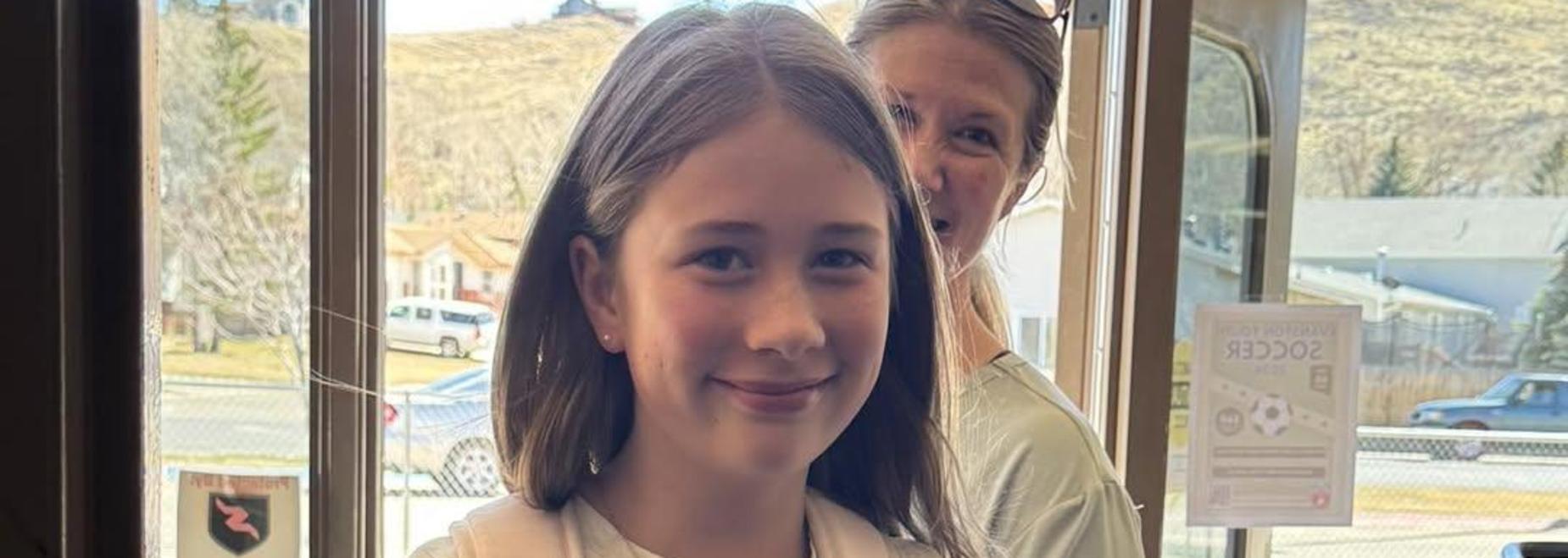 A young girl with a backpack smiles indoors.