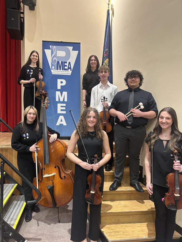 students dressed in black holding instruments in front of PMEA sign