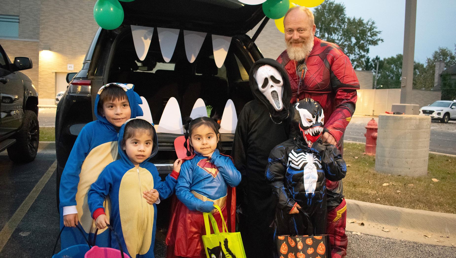 Group of children in various costumes with an adult in the background.