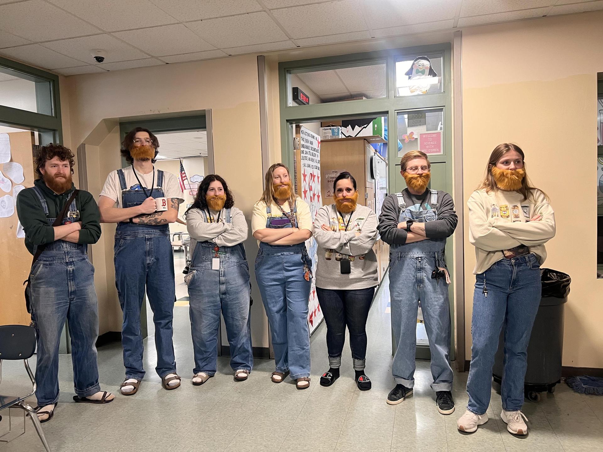Group of people with beards in a classroom posing confidently.