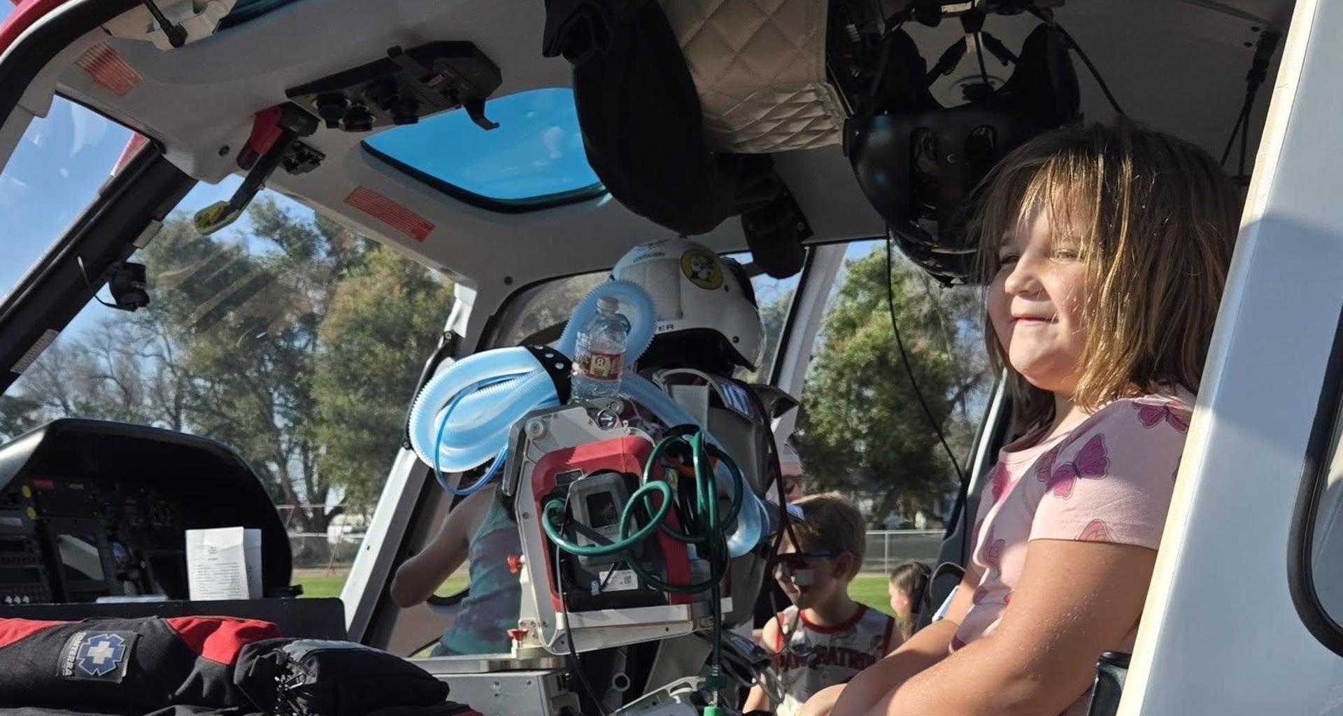 A child seated on an ambulance stretcher with medical equipment nearby.