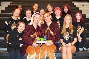 The colorguard team sits on the bleachers holding their award