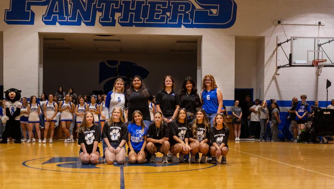 A group of students and coaches posing on a basketball court.
