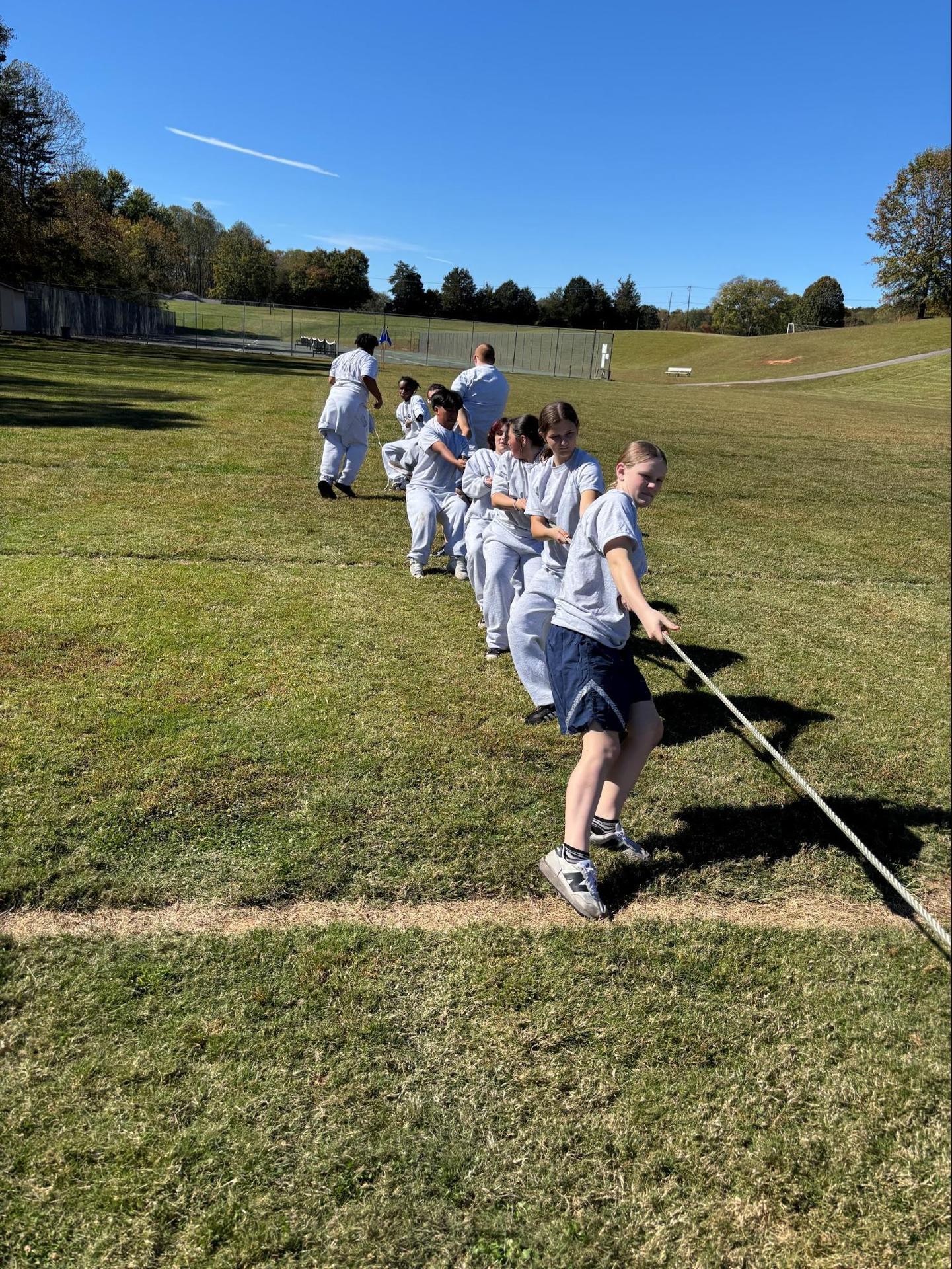Children participate in a tug-of-war game on a grassy field.