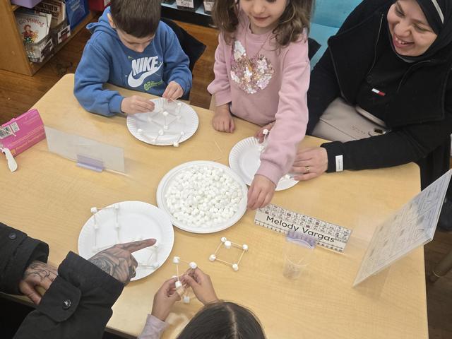 Children and adults building models with marshmallows and sticks at a table.