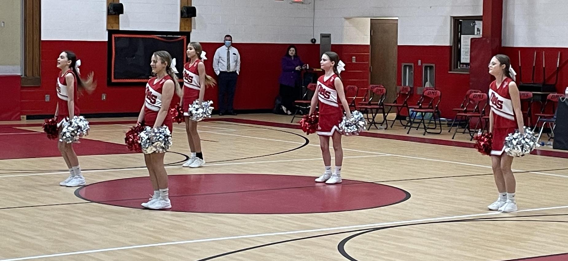Cheerleaders dance in a gym.