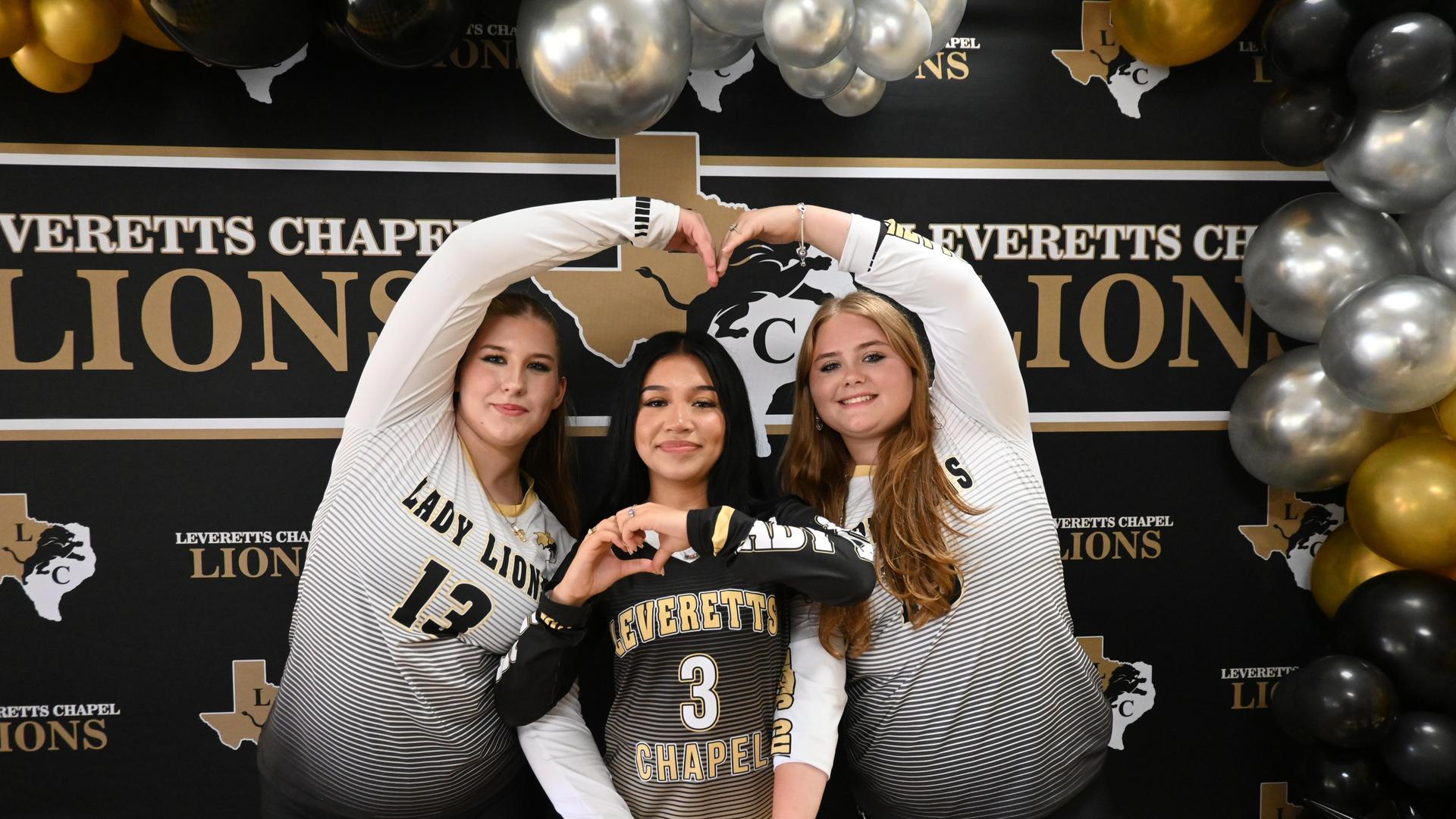 Three athletes in jerseys forming a heart shape with their hands.
