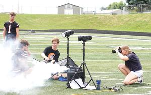 Two digital media students take photos of players on the field.