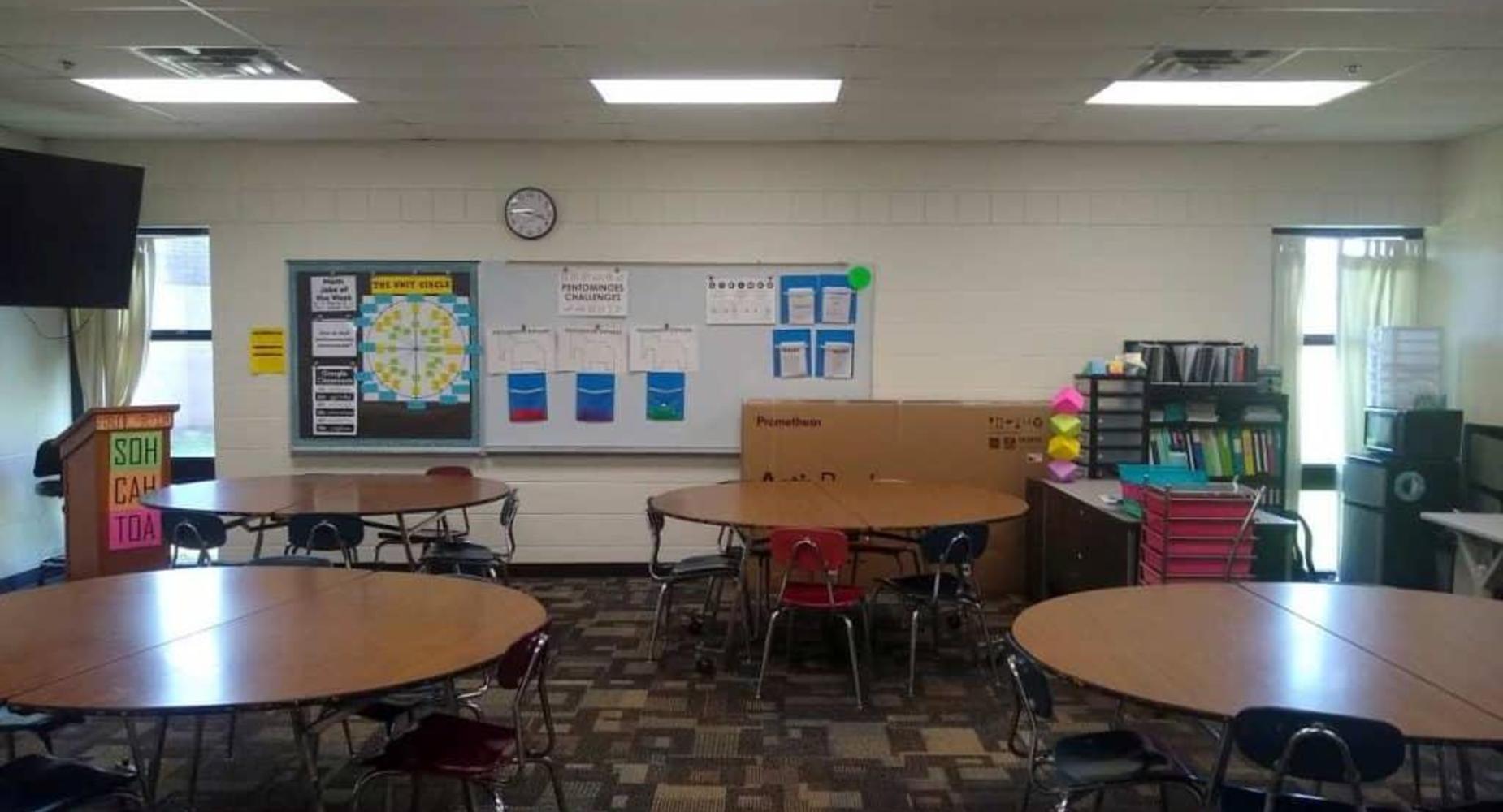 Classroom with round tables, chairs, bulletin board, and shelves.
