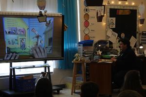 Dr. Suess book on screen with reader seated beside book