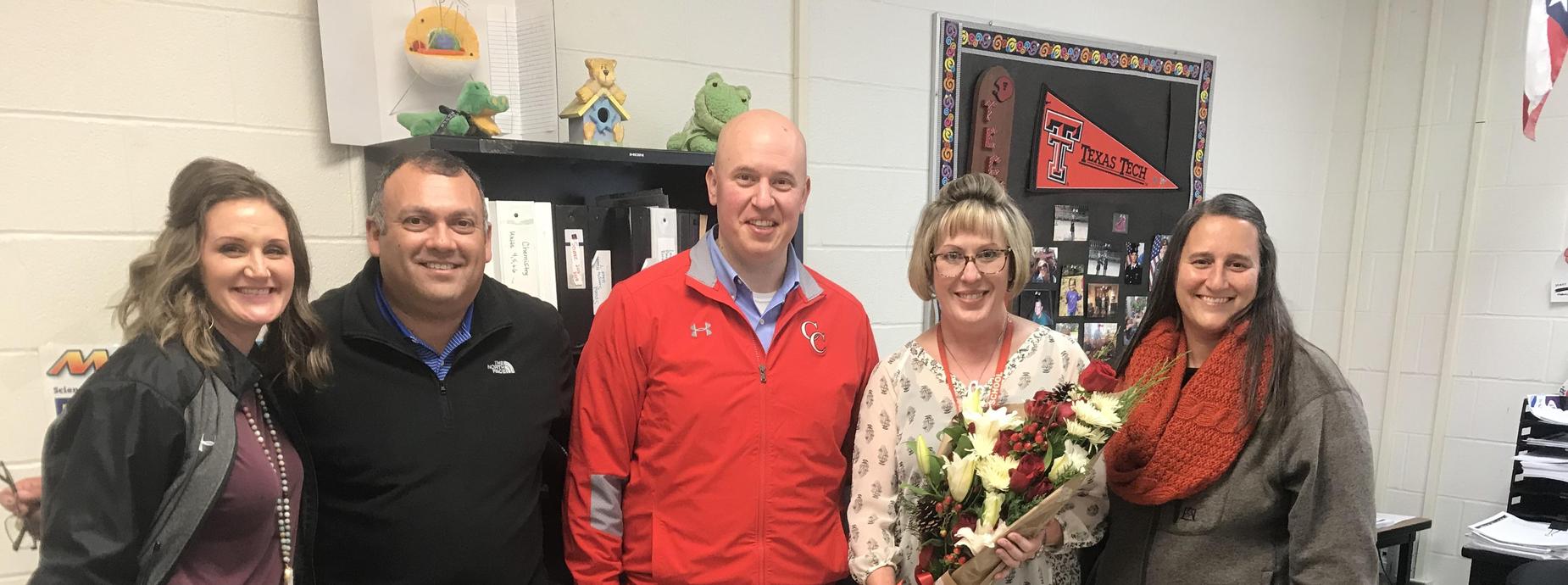 5 people standing together, one with a bouquet of flowers