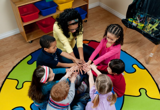 Children gathered in a circle, hands together on a puzzle-patterned rug.