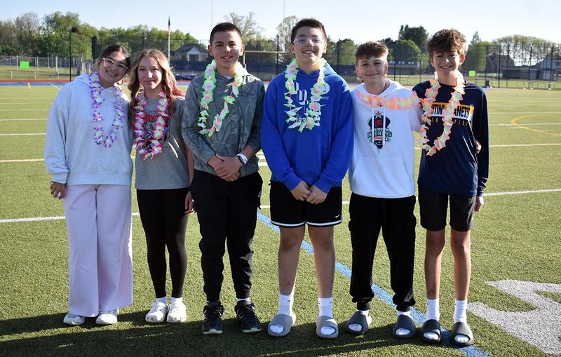 Five students in leis pose together on a sports field.