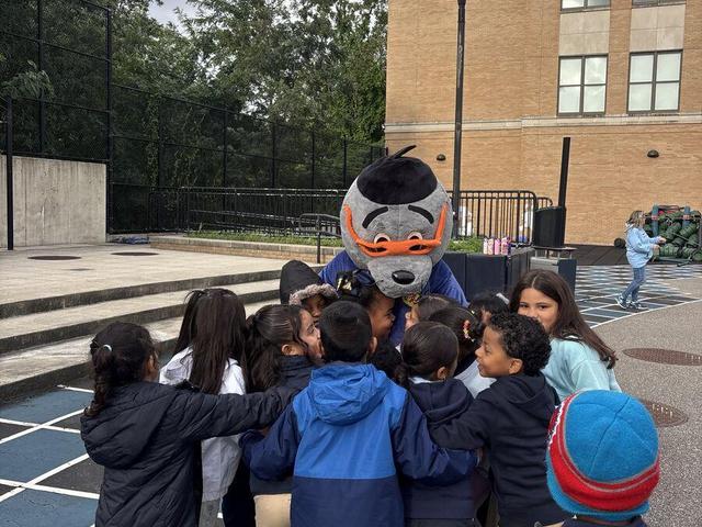 A group of children gathering around a mascot on a school playground.