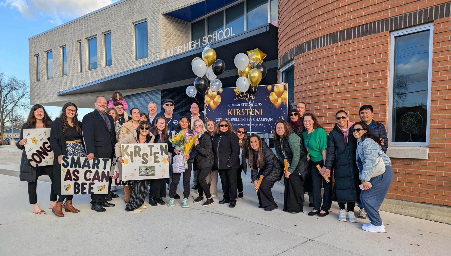 Celebration group with balloons and signs outside a school building.