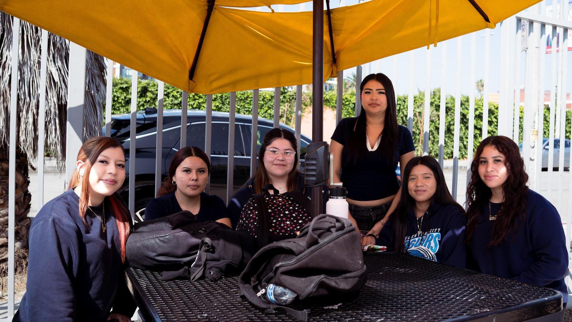 Six female students sitting together under a yellow canopy in an outdoor area.