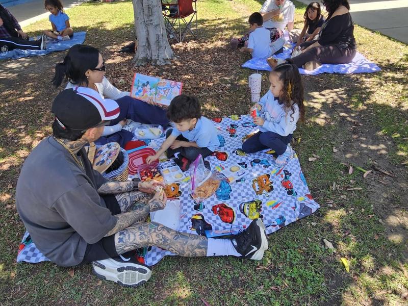 Children and adults enjoying a picnic on a blanket under a tree.
