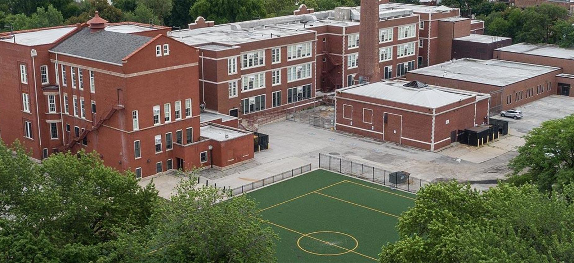 Aerial view of a school building with a green sports field in the foreground.