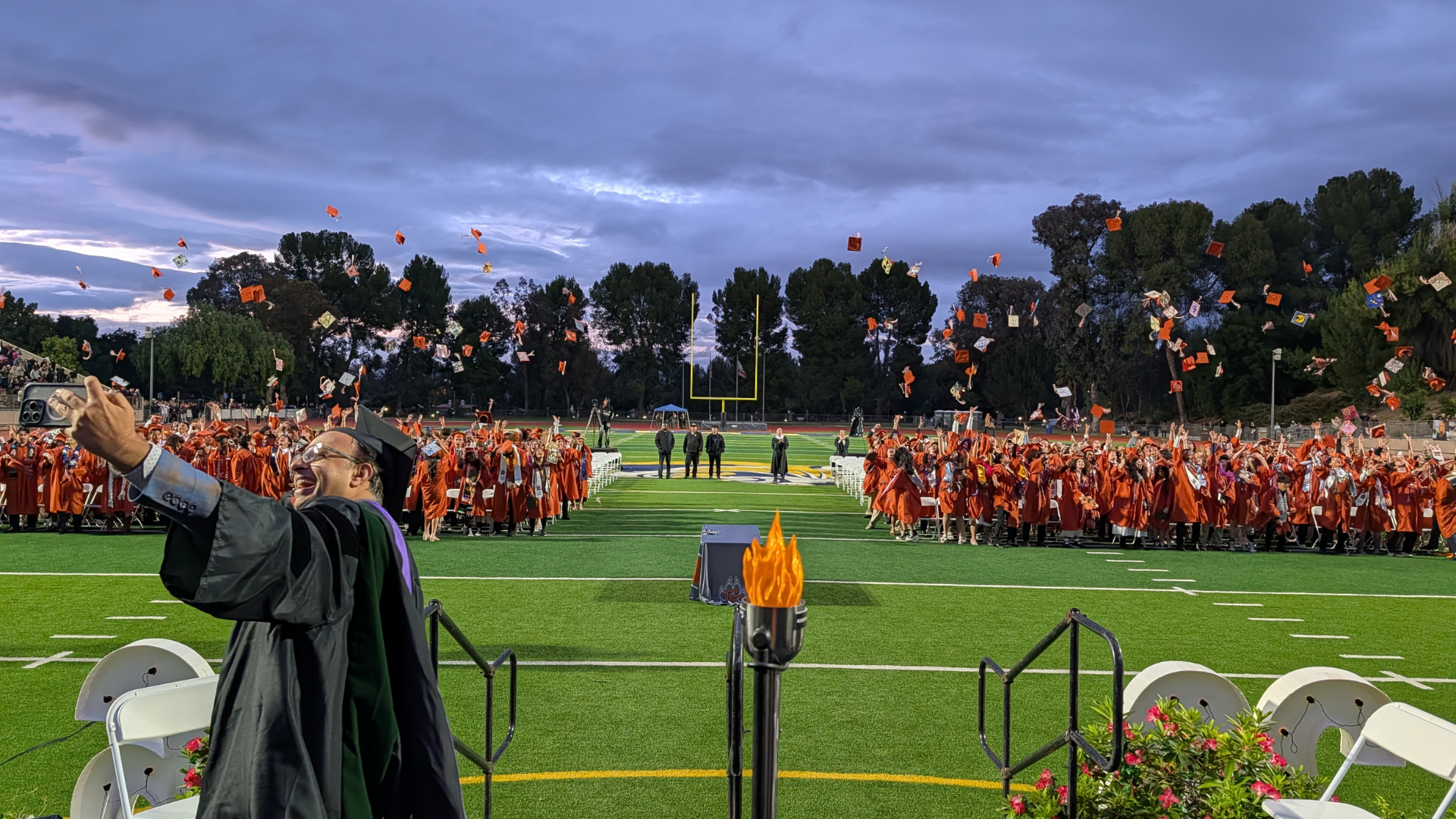 Graduates in orange gowns celebrating by tossing caps in the air.