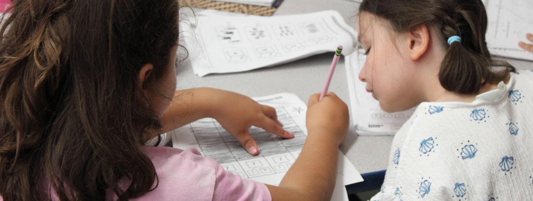 Two female elementary students doing paper and pencil math work together.