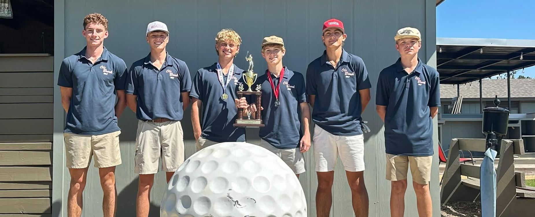 Six young men in matching shirts pose with a trophy and a large golf ball.