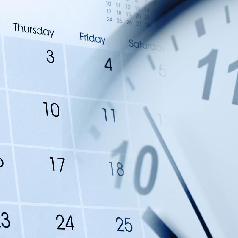Close-up of a calendar with blurred clock hands indicating time.