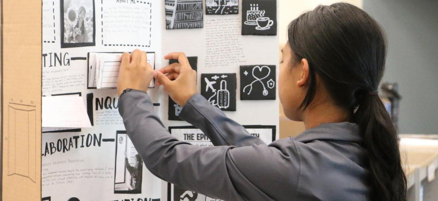 Student attaches notes to a presentation board covered with information.
