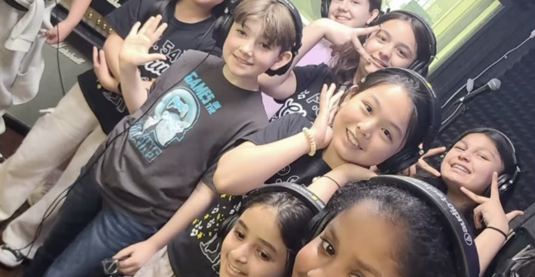 Group of children wearing headphones in a recording studio, smiling and posing.