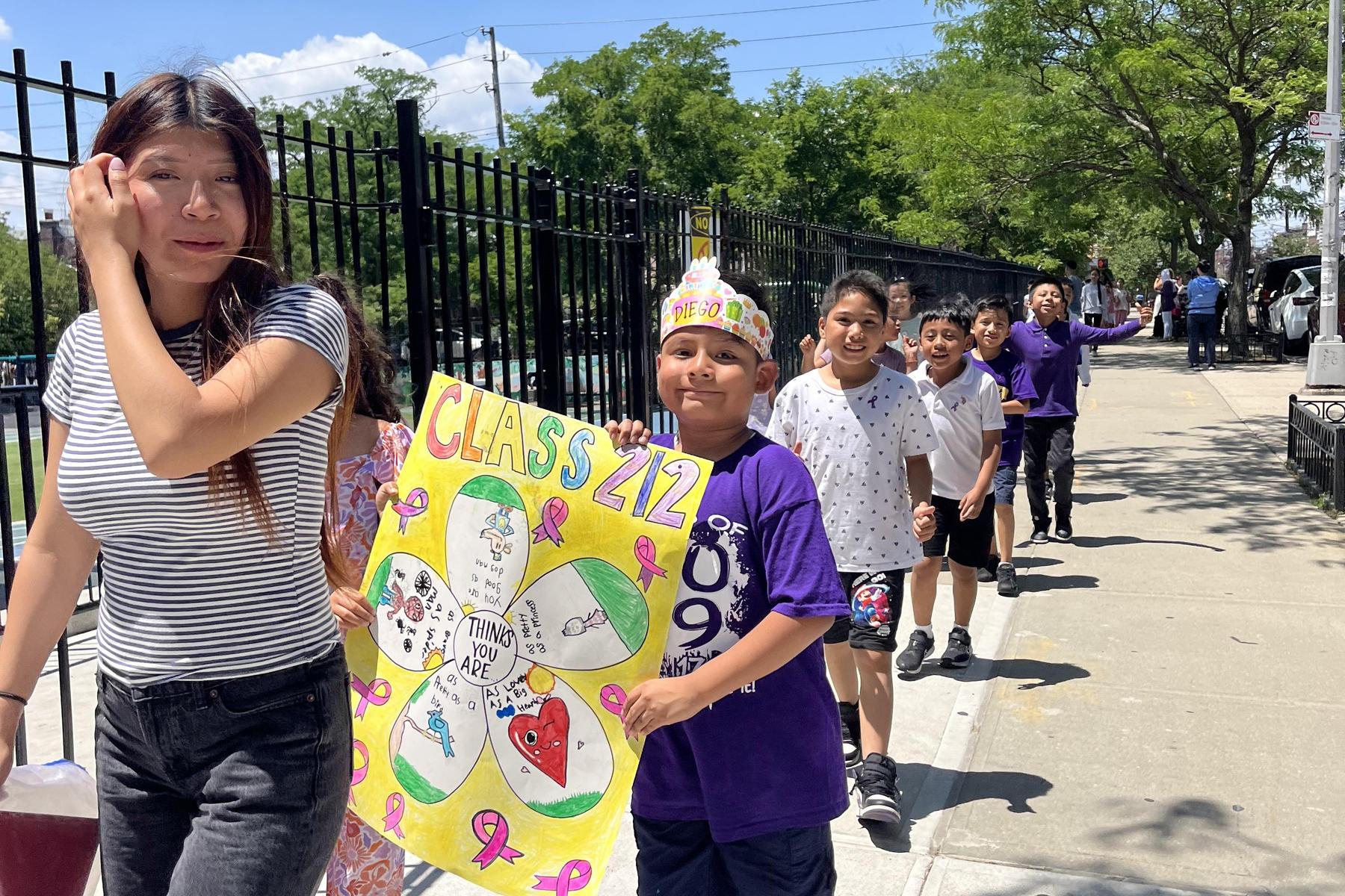 A group of kids in matching shirts and a crown, parading with a decorated poster.