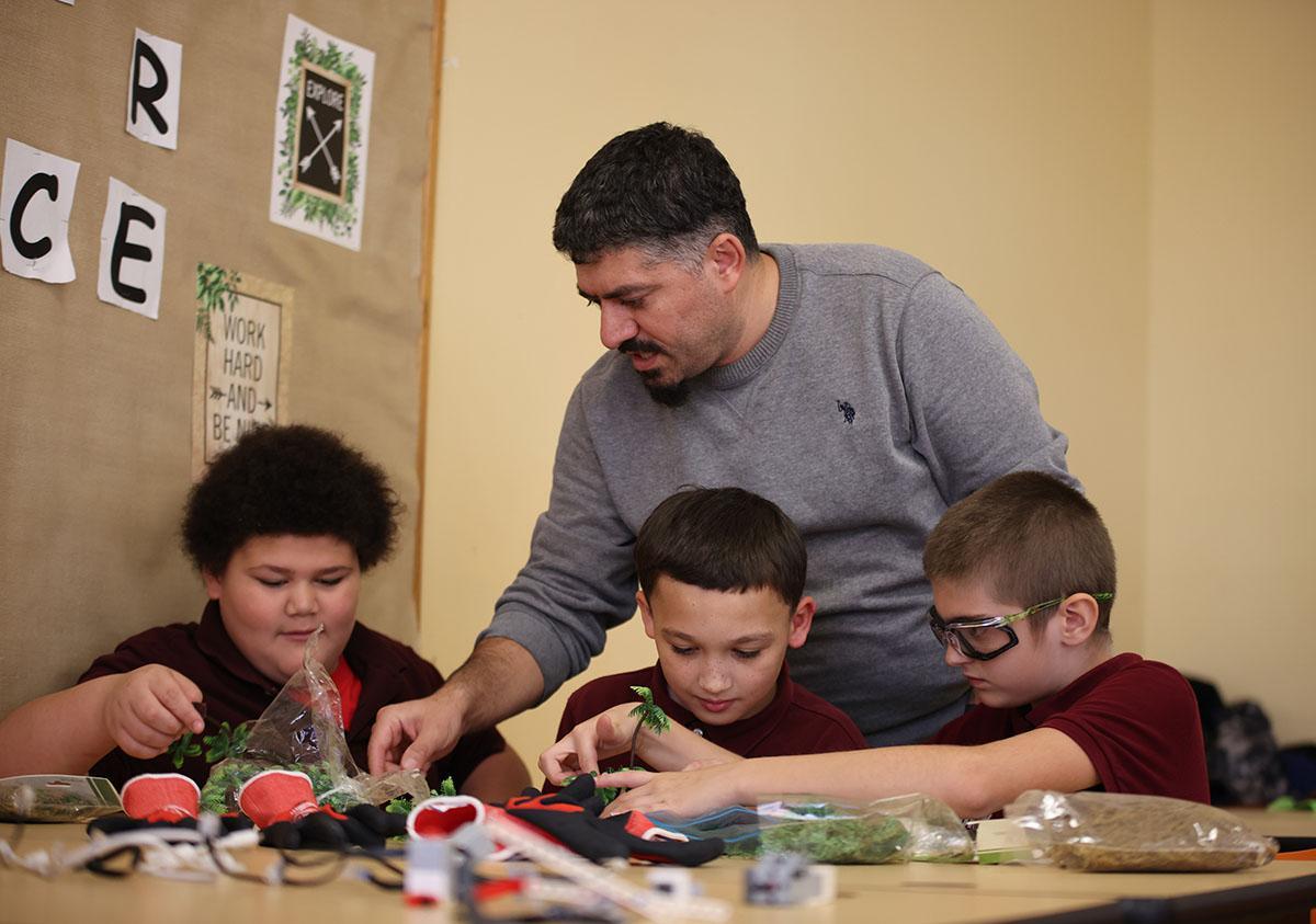 HSA Teacher smiles while kneeling beside a young student in a classroom setting.