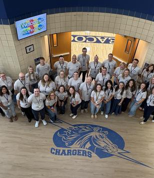 A group of smiling individuals in matching shirts gathers in a school entrance.