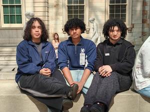 Three young people with curly hair sitting together outdoors.