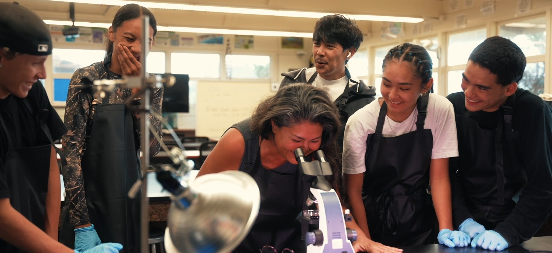 Students with science teacher looking into microscope