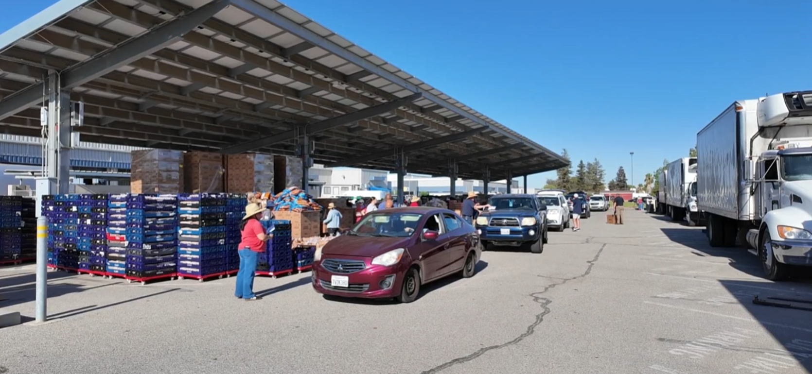 Crowd of people and vehicles at a market under a large roof structure.