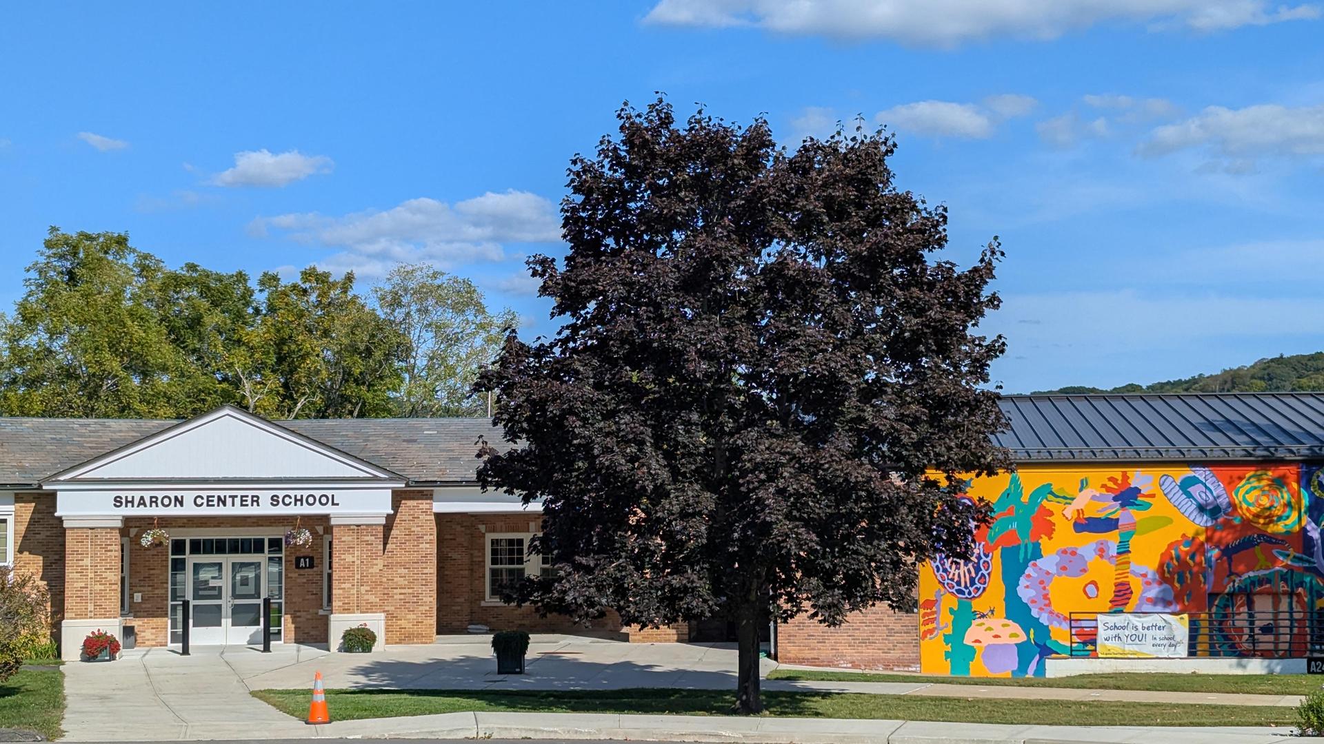 Front view of Sharon Center School with a large mural and a tree.