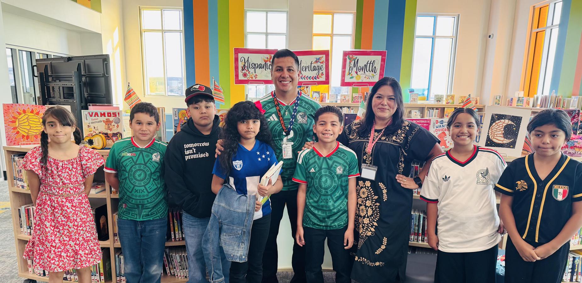 Group of children and adults in festive attire, standing in a library setting.