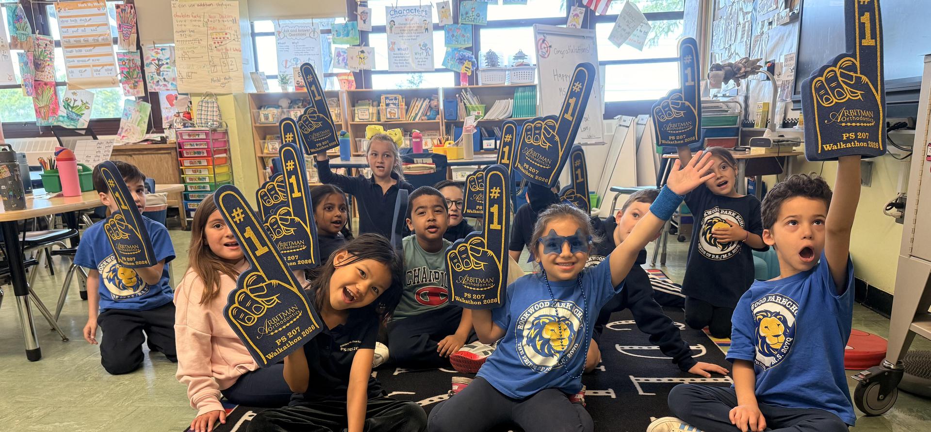 Children in a classroom holding up foam fingers and celebrating.