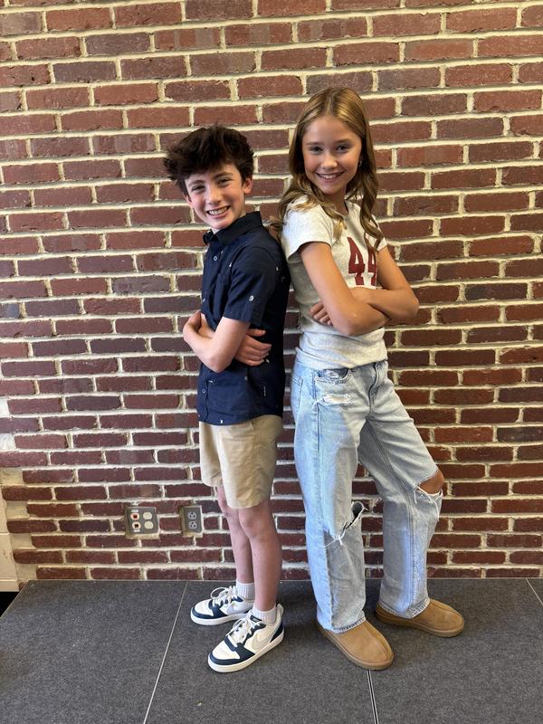 IMage depicts two students, one male, one female, standing back to back in front of a brick wall.
