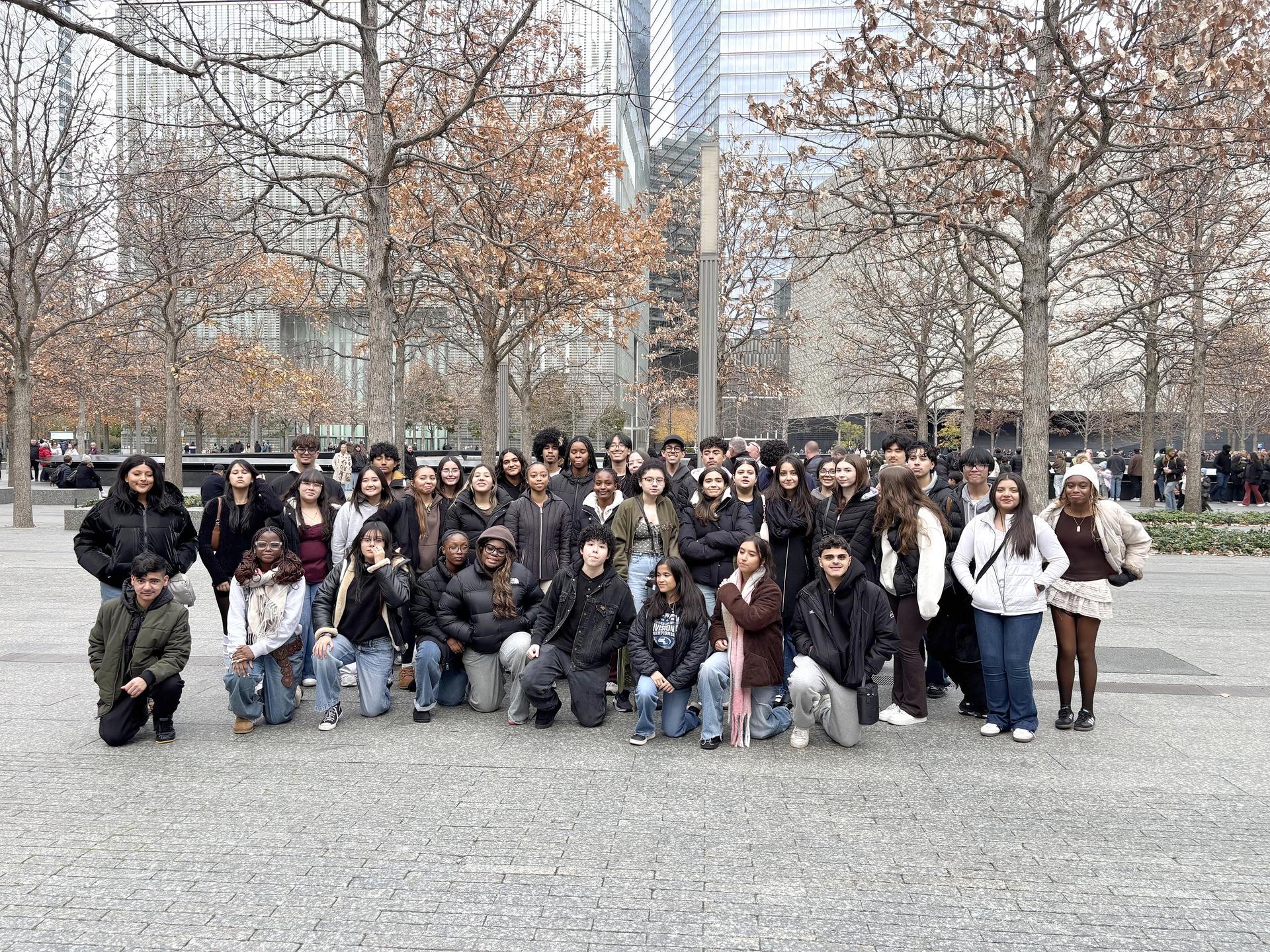 A large group of students poses together outdoors with trees and buildings in the background.
