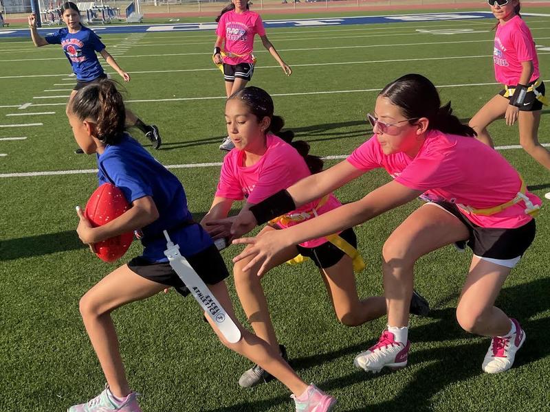 one girl runs with ball and two others try and take her flag