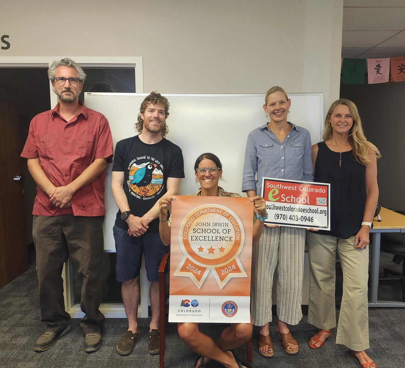 Group of five people posing with a School of Excellence banner and sign.