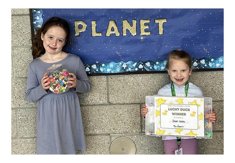 Two young girls, one holding a jar full of mini ducks and the other holding a certificate.